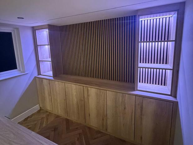 Fitted oak cabinetry with lit display shelving either side of a slatted wall panel